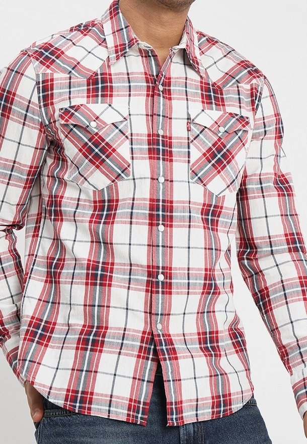 Homme portant une chemise à carreaux rouge, blanche et grise à manches longues avec boutons-pression et deux poches poitrine à l'avant.