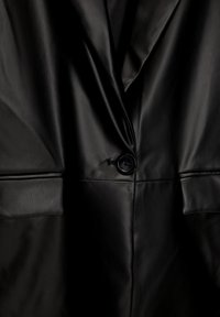 Blazer in pelle nera con revers a punta, chiusura a un bottone e ampie tasche frontali, caratterizzato da una texture liscia e lucida.