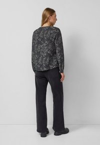 Koszula z długim rękawem o ciemnoszarej podstawie, z wzorem w panterkę w jaśniejszym szarym i czarnym kolorze. Połączona z luźnymi czarnymi spodniami.