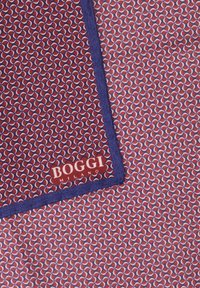 Zīda kabatas lakats ar sarkanu, baltu un zilu ģeometrisku rakstu, tumši zilu apmalīti un "BOGGI MILANO" zīmolu vienā stūrī.