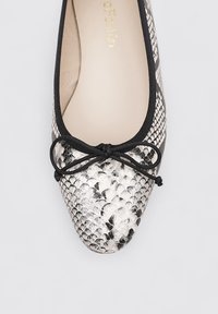 Chaussure plate avec un motif de serpentin noir et blanc brillant. Elle présente un bout rond, des bordures noires et un nœud décoratif à l'avant.