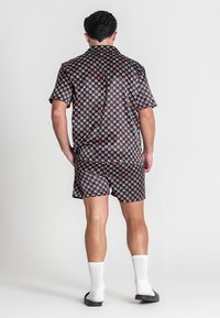 Kurzes Shirt und Shorts Set in Schwarz mit einem geometrischen Muster aus Quadraten in Pink, Rot und Weiß. Das Material wirkt glatt.