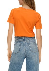Oranje katoenen t-shirt met een ronde hals, korte mouwen en een ontspannen pasvorm, gecombineerd met hooggesneden lichtgewassen denim jeans.