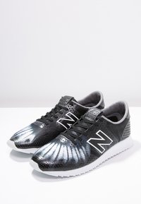 Chaussures de course noires et grises avec une tige à motifs, affichant un logo "N" blanc bien visible, des superpositions texturées et une semelle en caoutchouc blanche.