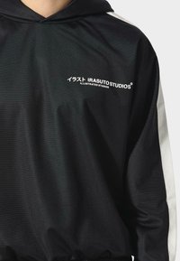 Felpa nera con cappuccio e accenti bianchi, tessuto liscio, presenta il logo "IRASUTO STUDIOS" in bianco e caratteri giapponesi sul davanti.