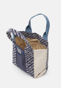 Mała torebka na ramię w wielokolorowym materiale z niebieskimi i beżowymi panelami, z nadrukowanym napisem "See By Chloé" oraz dwoma uchwytami na białym tle.