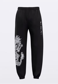 Zwarte joggingbroek met een elastische tailleband, voorzien van een grote witte draak afbeelding aan één zijde en kleine Japanse tekst langs het been.
