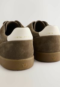 Braune Wildledersneaker mit cremefarbenen Fersenakzenten. Texturiertes Obermaterial, Gummisohle mit markantem Kronenlogo. Minimalistisches Design mit goldener Beschriftung.