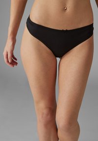 Zwarte katoenen bikini slipjes met een gladde textuur, voorzien van een delicaat strikaccent aan de voorkant en een golvende tailleband.