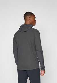Haut à manches longues de sport en gris foncé avec un tissu texturé, un design ajusté et une capuche. Présente des manches et des accents latéraux plus foncés en contraste.