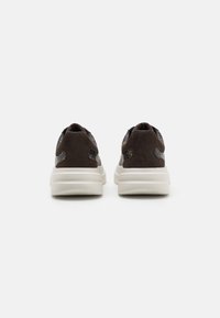 Mørkebrune semskede sneakers med et teksturert mønster, med en tykk hvit såle og subtil merkevare på sidene, sett fra baksiden.