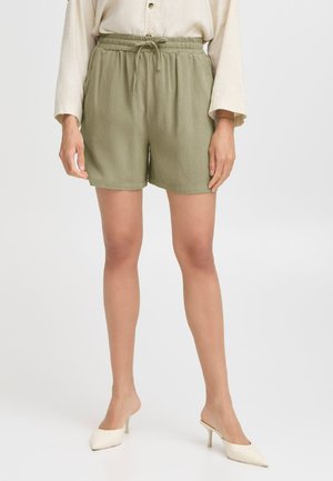 Olive green, elastic-waist shorts with a drawstring, featuring side pockets and a lightweight, textured fabric. Paired with cream heels.
