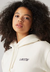 Ljusgrå hoodie med dragkedja, med broderad "LEVI'S®" logotyp på vänster bröst. Mjukt material, avslappnad passform.