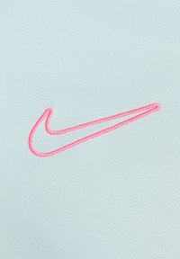Svijetloplava atletska tkanina s mekim teksturom, na kojoj se nalazi ružičasti izvezeni Nike swoosh logo.