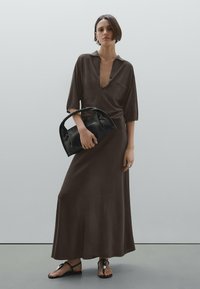 Brown maxi dress with a collar and button detail, paired with a black leather handbag and flat sandals, showcasing a smooth, flowing texture.