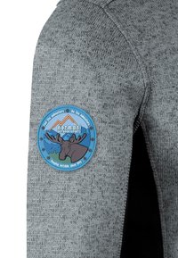 Grå, stickad tyg med en texturerad yta; har ett cirkulärt, färgglatt logotyget med en älg och berg.