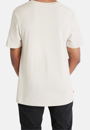 Man met een eenvoudige witte T-shirt met korte mouwen en een zwarte broek, gezien van achteren met zichtbare getatoeëerde armen.