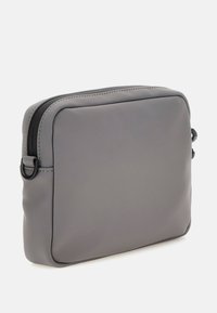 Bolsa rectangular gris hecha de material sintético suave. Presenta un cierre de cremallera y bordes redondeados, con un diseño minimalista y detalles en negro.
