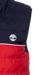 Pohodlný puffer vest v námořnické modré a červené barvě se skládá z různobarevných bloků, s vysokým límcem, bílým logem a horizontálním prošíváním. Měkká, izolační textura.