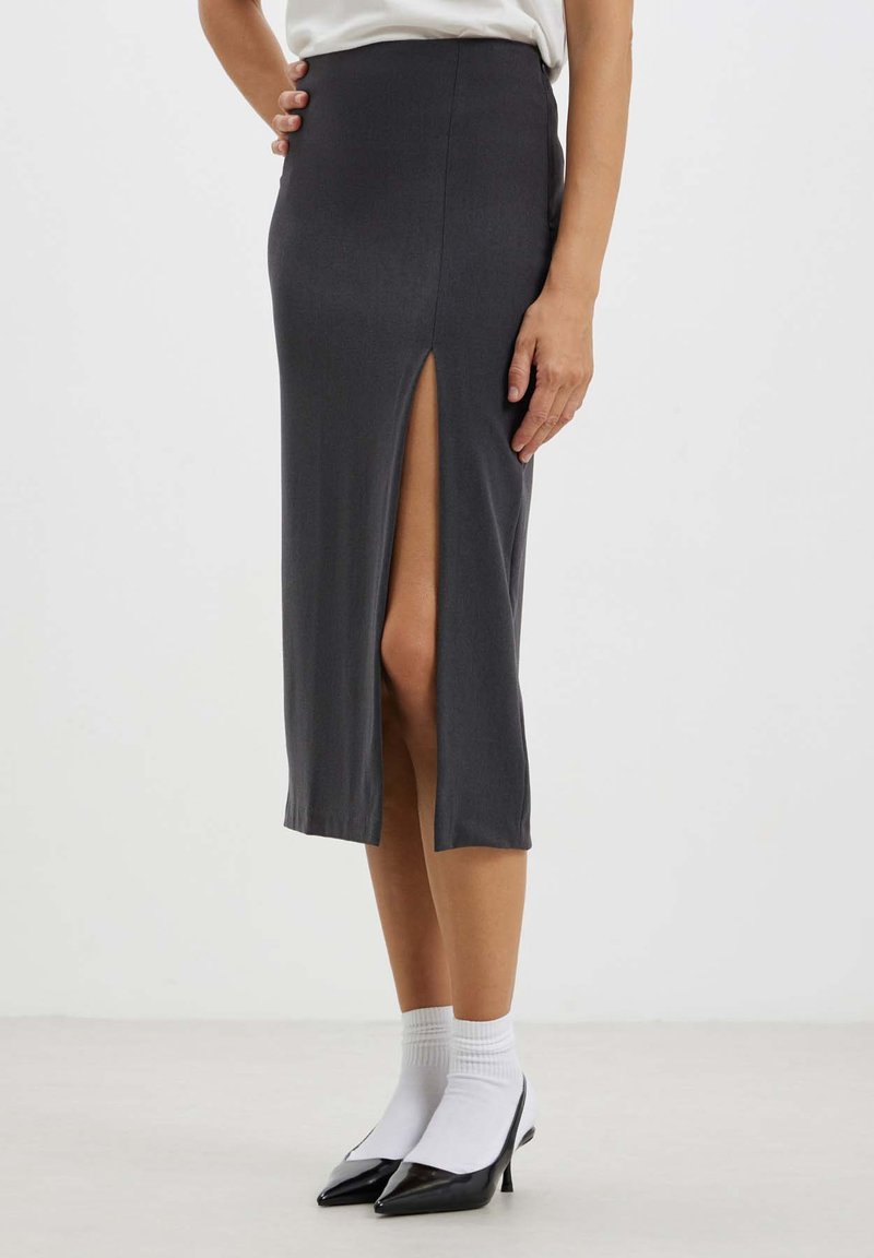 Jupe midi gris foncé avec une fente sur le côté, fabriquée en tissu lisse. Le design présente une taille cintrée et une coupe droite, associée à des escarpins noirs pointus.