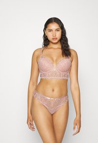Conjunto de lingerie rendada em rosa suave com bordas recortadas, apresentando um sutiã com um detalhe central em metal e uma tanga de cintura baixa correspondente.