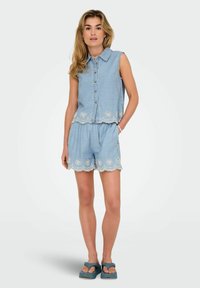 Jeans bez rukava sa zatvaranjem na dugme, s čipkastim detaljima. Odgovarajuće jeans šortse imaju obrubljene čipkaste detalje. Plava boja, opušteni kroj, svakodnevni dizajn.