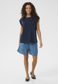 Tengerészkék, rövidujjú felső világoskék, kockás mintázatú rövidnadrággal párosítva. Lapos, fekete cipők teszik teljessé a lezser öltözéket.