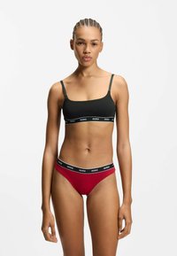 Sort bralette med justerbare stropper og logo-bånd, kombineret med røde bikiniunderdel med et tilsvarende logo-bånd, glat stof.