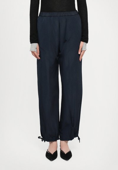 Pantalones azul marino, livianos, de cintura elástica con puños ajustables y bolsillos laterales, combinados con unas bailarinas negras de punta.
