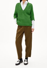 Pull en tricot vert avec un col en V et des manches courtes, associé à un pantalon marron ajusté et des mocassins noir et blanc.