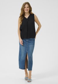 Haut sans manches noir avec un détail de bouton, associé à une jupe en jean bleu avec une fente à l'avant, et des sandales à talons bleu clair.