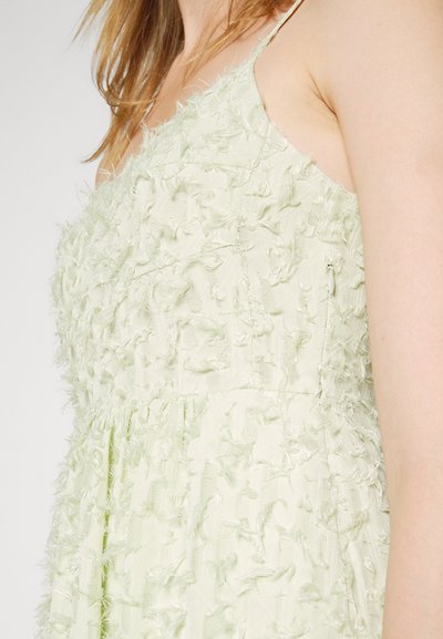Vestido verde claro com um tecido texturizado e detalhes desfiados. Alças finas e corpete ajustado. Saia suave e esvoaçante.