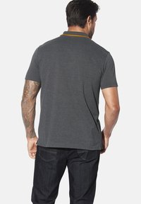 Graues Poloshirt mit einem kontrastierenden gelben Kragen, kurzen Ärmeln und einer glatten Textur. Getragen mit dunklen Denim-Jeans.