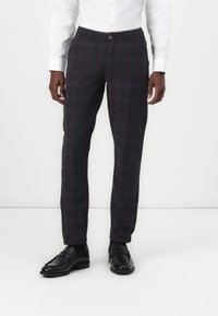 Pantalones de cuadros gris oscuro, con una cintura relajada, detalles rojos en el patrón de cuadros y un diseño ajustado. Combinados con mocasines negros.