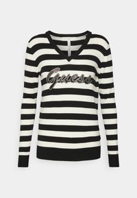 Pull rayé noir et blanc avec un col en V, orné d'un logo "Guess" en strass à l'avant. Manches longues et poignets côtelés.