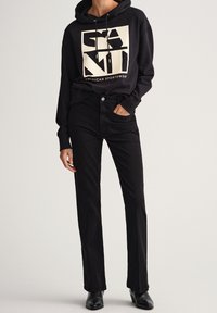 Sudadera negra con un logo geométrico crema, combinada con pantalones rectos negros y botines negros. Tejido suave, corte relajado.