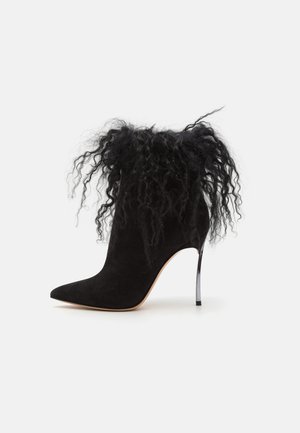 Sort ruskind ankelstøvle med spids tå, udsmykket med krøllet sort pels i toppen og en stilettohælhæl med metallisk finish.