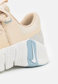 Talons de baskets beige et blanc cassé avec une semelle blanche épaisse comportant un détail du logo swoosh bleu et blanc sur le côté.