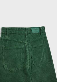 Pantalon en velours côtelé vert foncé vu de dos avec deux poches arrière et un petit patch de marque sur la ceinture.