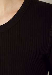 Il tessuto a coste nere presenta un collo rotondo e un design delle spalle senza cuciture, mostrando una texture morbida e una leggera lucentezza.