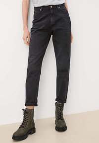 Czarne dżinsy z wysokim stanem i zwężanymi nogawkami. Noszone z zielonymi wojskowymi butami na sznurowadła z masywną podeszwą.