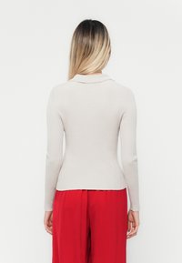 Tett, lyse beige ribbestrikket topp med krage, lange ermer og en lett utflaring i kanten, kombinert med løse røde bukser.