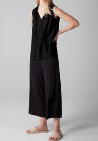Top negro sin mangas con escote en V y cinturilla fruncida, combinado con culottes negros de corte holgado y sandalias tipo slide en rosa claro.