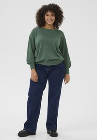 Grön, löst sittande stickad tröja med bred halsringning och långa ärmar, som är ihopparad med mörkblå raka jeans och svarta platåskor.