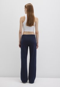 White ribbed crop top paired with high-waisted, wide-leg navy pants, featuring a smooth texture and a classic design.
