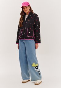 Čierna prešívaná bunda s ružovými akcentmi a kvetinovými vzormi; voľné modré džinsy s kreslenou postavičkou; ružová čiapka; biele tenisky.