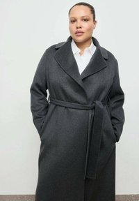 Cappotto di lana grigio con ampio colletto, fronte senza bottoni e vita con cintura. Dotato di due tasche laterali e vestibilità rilassata e oversize.