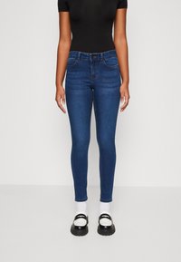 Calças de ganga azul finas com cintura média, design de cinco bolsos e costura subtil. Combinadas com sapatos de plataforma preto e branco.