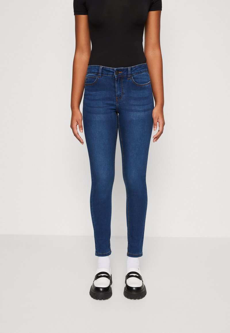 Calças de ganga azul finas com cintura média, design de cinco bolsos e costura subtil. Combinadas com sapatos de plataforma preto e branco.