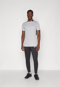 Γκρι κοντομάνικο αθλητικό μπλουζάκι με μαύρη λεπτομέρεια, συνδυασμένο με μαύρο στενό παντελόνι και μαύρα αθλητικά παπούτσια. Ο λογότυπος της Nike ορατός και στα δύο κομμάτια.